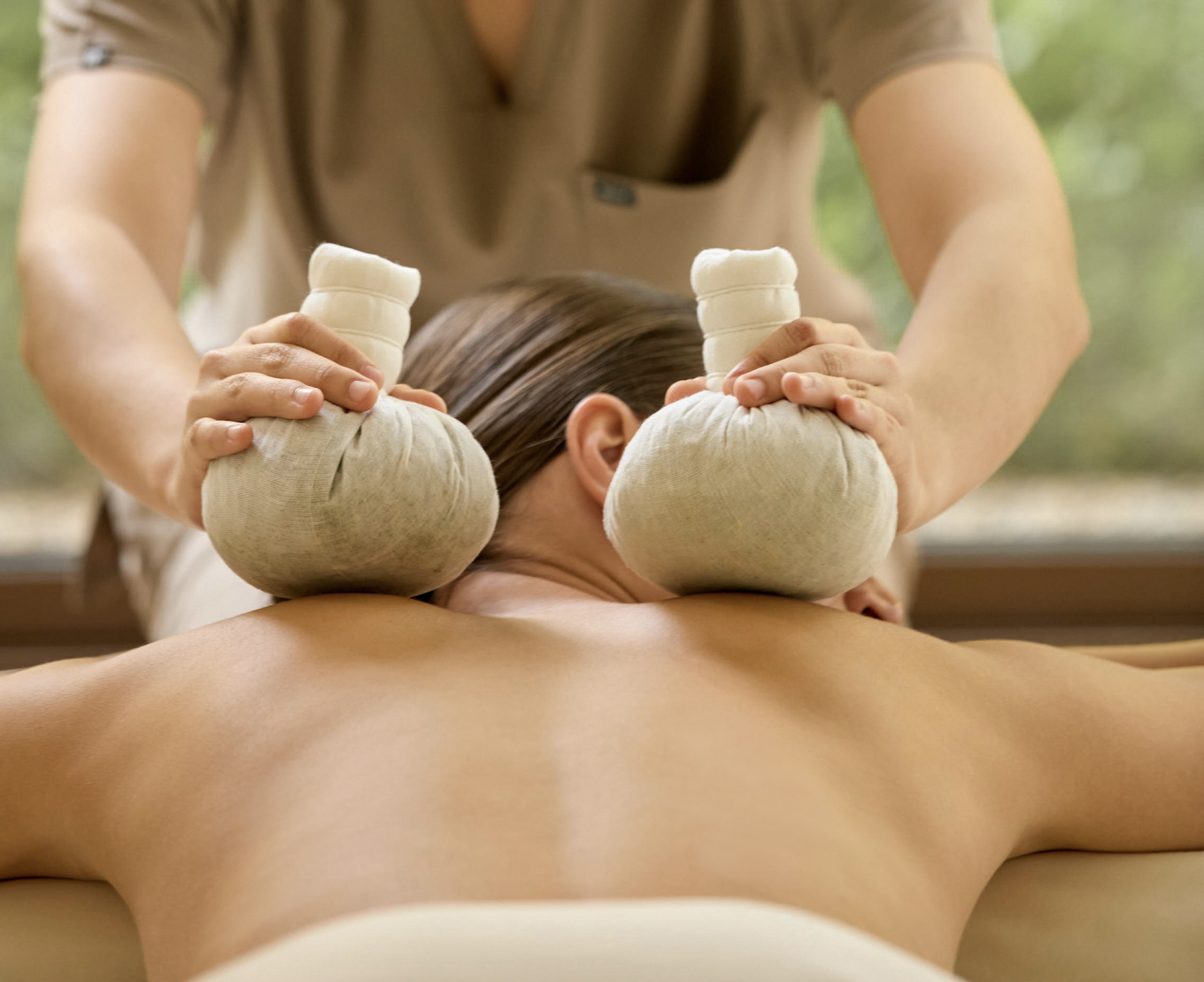 Wellness jai - en kvinna ger en annan kvinna massage med två kompresser på ryggen.